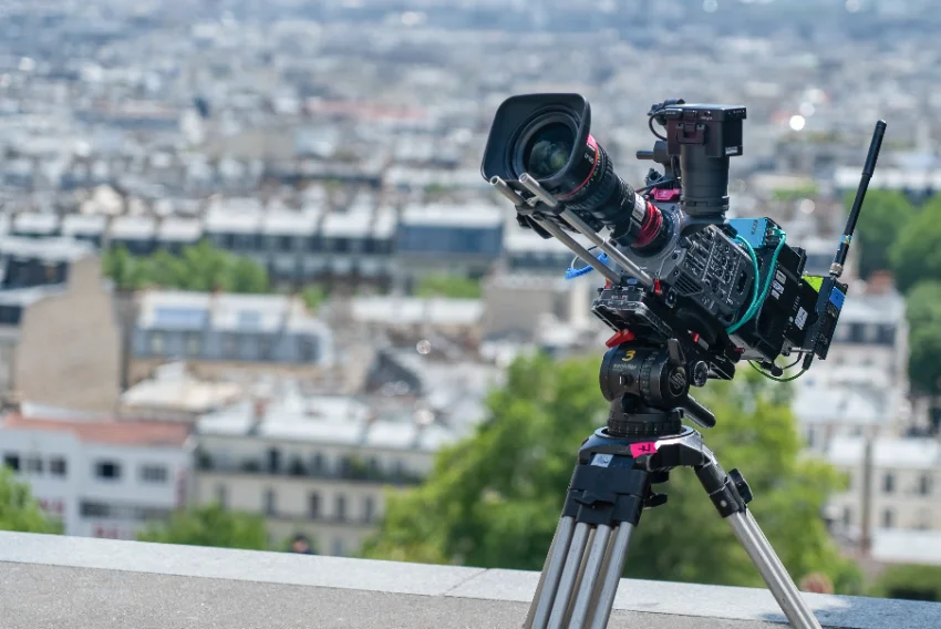 Large-sensor cinema camera on a fluid-head tripod overlooking a city rooftop skyline