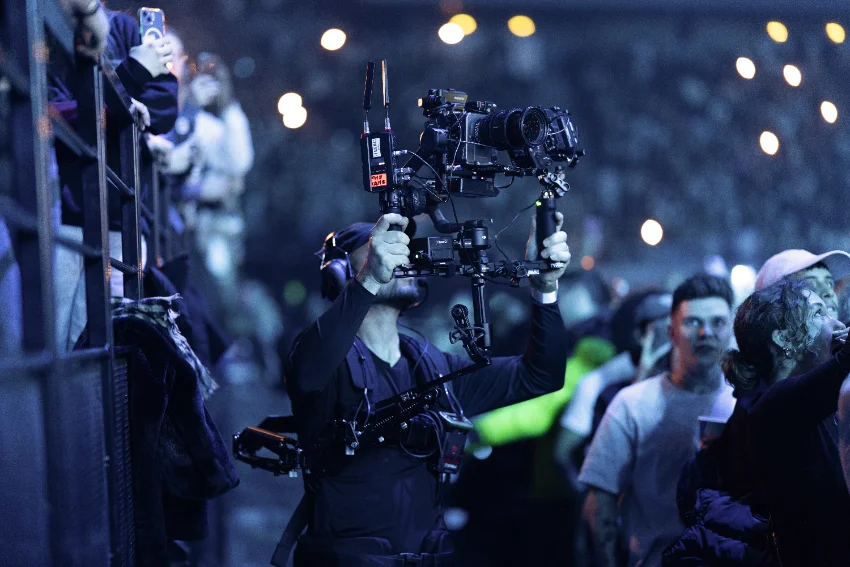 Operator carrying a gimbal-mounted camera rig through a stadium crowd at night
